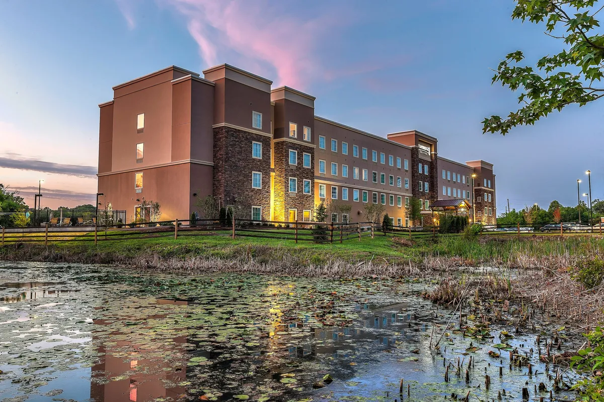 A tranquil outdoor scene featuring the building beside a peaceful pond, with picturesque sky reflections at sunset. The setting provides a restful retreat after a day spent exploring nearby attractions, emphasizing the balance between activity and relaxation.