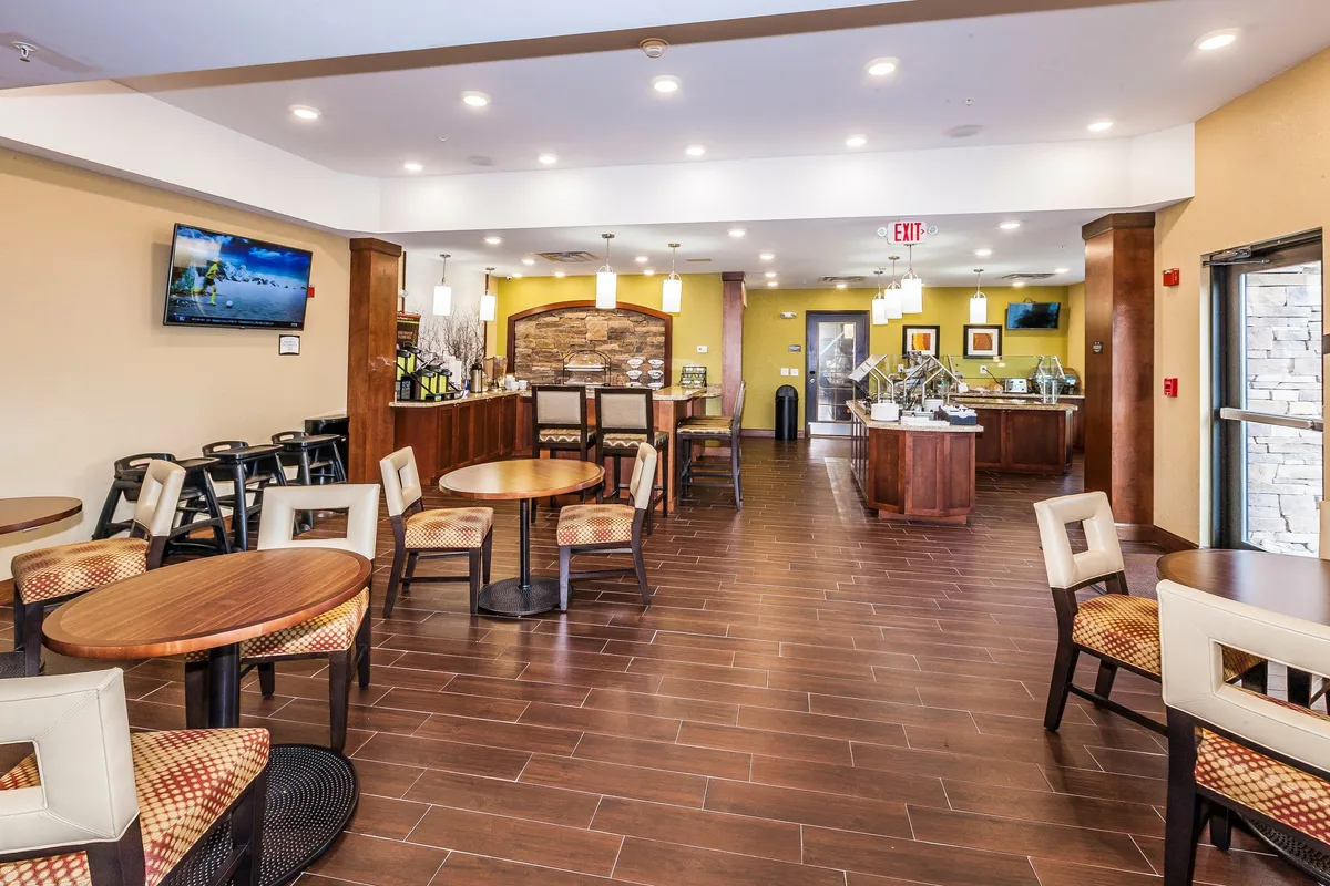 A cozy interior lobby space featuring a central seating area, a modern reception desk, a wall-mounted TV, and a stylish decorative stone wall. Guests can be seen socializing, enjoying light bites, or working on laptops, highlighting the versatility of the space for both relaxation and evening receptions.