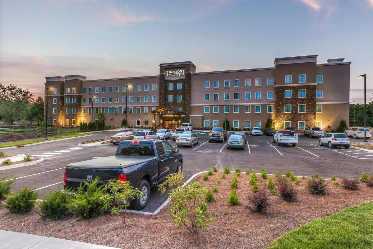 This exterior image highlights the welcoming hotel entrance surrounded by thoughtfully landscaped gardens and a convenient parking area. The scene is bathed in soft sunset light, inviting guests to arrive or depart with ease. The proximity to the entrance underscores the accessibility to nearby shops and dining options.