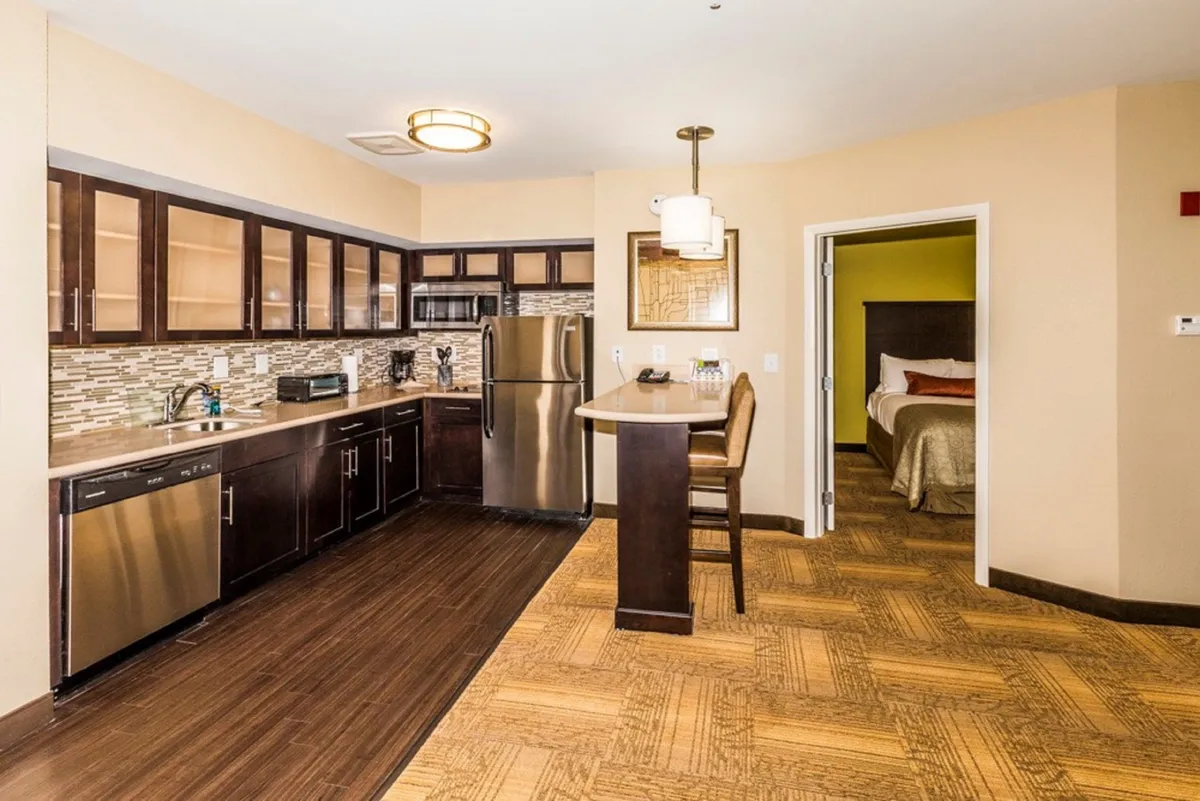 This image features a modern kitchen with a spacious counter, stainless steel appliances including a stove and refrigerator, and bar stools that encourage both cooking and casual dining. The inviting setup hints at meal preparation, entertaining guests, and informal breakfasts at the counter.