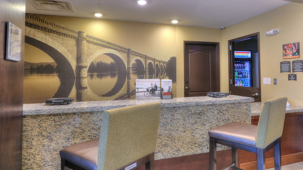 The image shows a welcoming interior space featuring a granite countertop, an impressive mural of an arched bridge that adds a sense of local character, and a comfortable seating area. Guests are engaged in activities like checking in, relaxing before departure, or planning upcoming excursions. The ambiance is inviting and serene, setting the tone for memorable adventures and moments of relaxation.