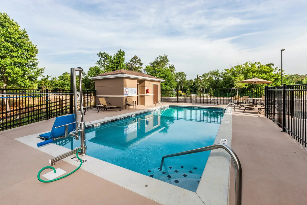 A sparkling outdoor swimming pool surrounded by comfortable lounge chairs and shade umbrellas. In the background, a pool house sets the scene for both sunbathing and lively gatherings, while the inviting water beckons guests to cool off. The area is filled with natural light, emphasizing relaxation and fun, whether guests are taking a quiet morning dip or joining friends for a festive poolside event.